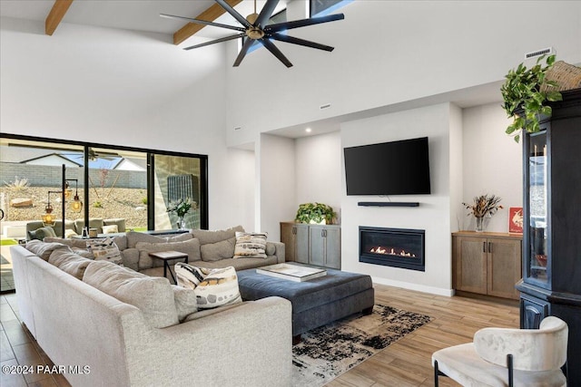 living room with beamed ceiling, ceiling fan, a towering ceiling, and light hardwood / wood-style flooring