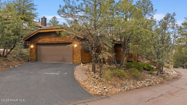 view of front of house with aphalt driveway, a chimney, and an attached garage