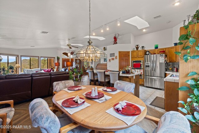 dining space featuring lofted ceiling with skylight, visible vents, ceiling fan with notable chandelier, and rail lighting