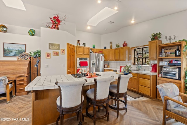 kitchen featuring tile countertops, a kitchen island, a skylight, stainless steel appliances, and decorative backsplash