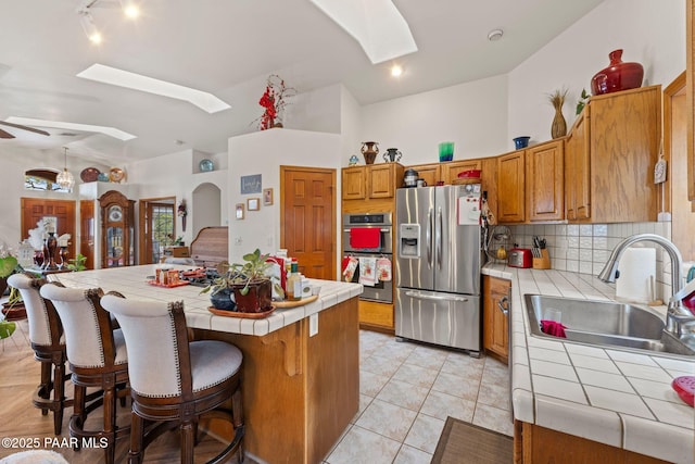 kitchen with ceiling fan, tile counters, lofted ceiling with skylight, appliances with stainless steel finishes, and a sink