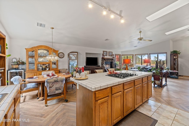 kitchen with visible vents, stainless steel gas cooktop, a stone fireplace, tile counters, and open floor plan