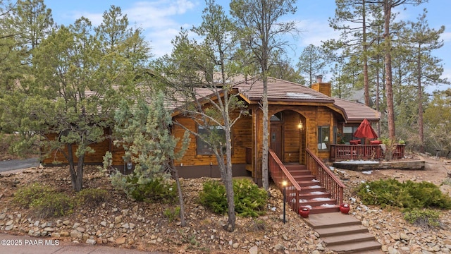 view of front of house with stairs, a tile roof, a porch, and a chimney