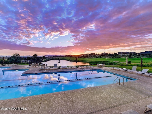 pool at dusk featuring a water view and a patio