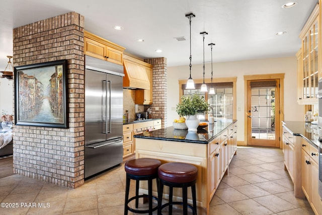 kitchen with built in refrigerator, pendant lighting, a breakfast bar area, light brown cabinetry, and a kitchen island