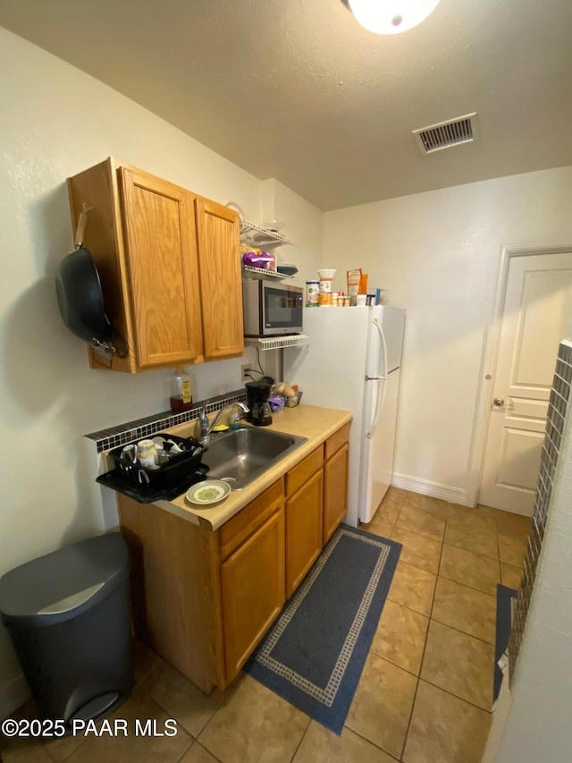 kitchen featuring light tile patterned floors, brown cabinetry, visible vents, a sink, and stainless steel microwave