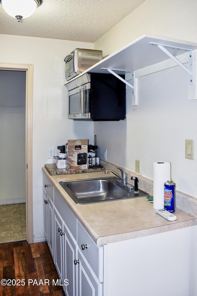 kitchen with a textured ceiling, dark wood-type flooring, light countertops, and a sink