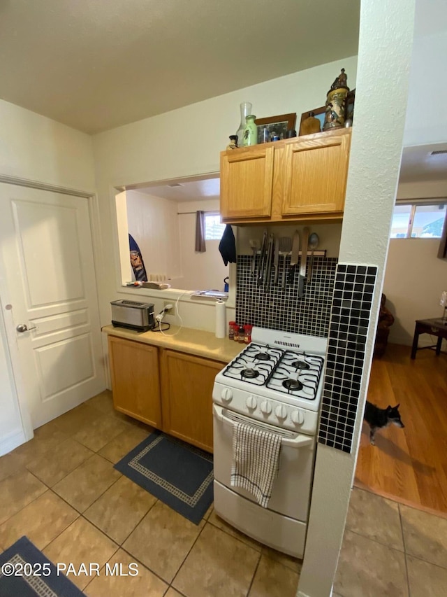 kitchen featuring light tile patterned floors, white range with gas cooktop, light brown cabinets, and light countertops