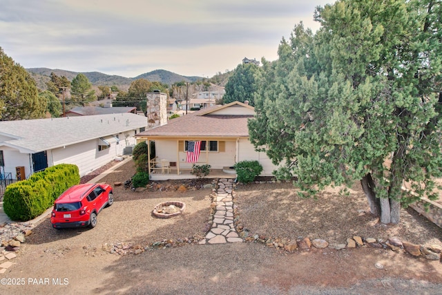 ranch-style home with a mountain view, covered porch, a chimney, and an outdoor fire pit