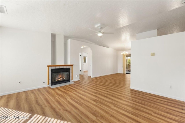 unfurnished living room featuring hardwood / wood-style flooring, vaulted ceiling, a textured ceiling, and a tiled fireplace