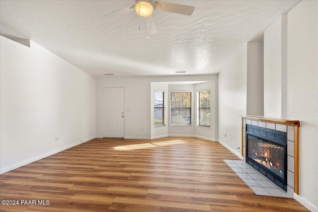 unfurnished living room featuring wood-type flooring, a textured ceiling, ceiling fan, and a tiled fireplace