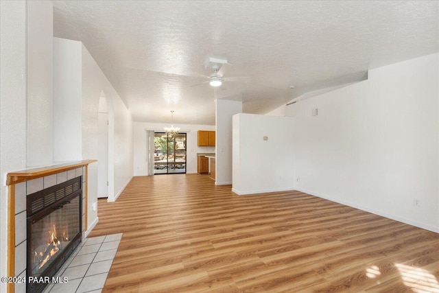 unfurnished living room with a fireplace, ceiling fan with notable chandelier, a textured ceiling, and light wood-type flooring