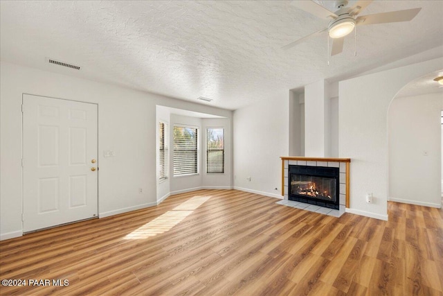 unfurnished living room with a textured ceiling, light wood-type flooring, ceiling fan, and a tiled fireplace