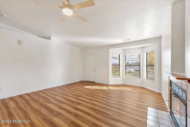 empty room with a fireplace, light wood-type flooring, and a textured ceiling