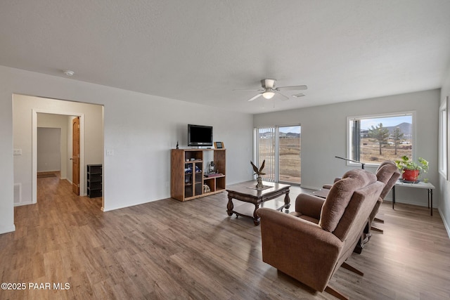 living room with ceiling fan, light hardwood / wood-style flooring, and a textured ceiling