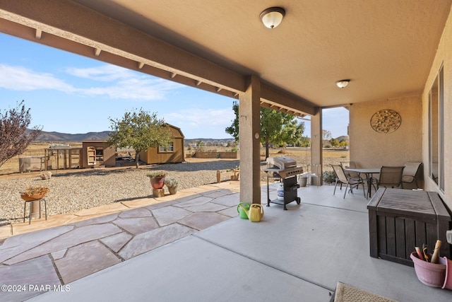 view of patio with a mountain view, a storage unit, and a grill