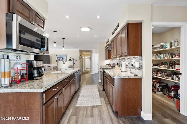 kitchen featuring light stone countertops, sink, hanging light fixtures, stainless steel appliances, and hardwood / wood-style flooring