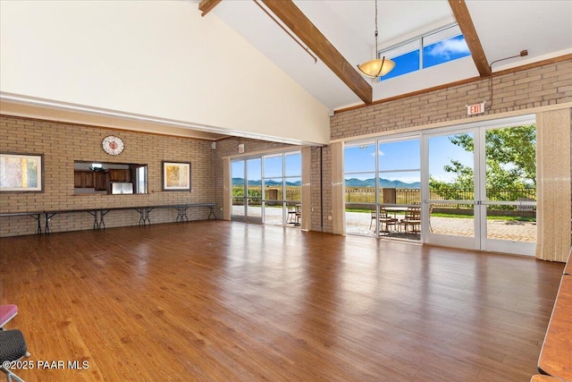 unfurnished living room with a mountain view, beam ceiling, high vaulted ceiling, and brick wall