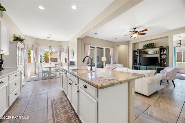 kitchen with white cabinetry, sink, decorative light fixtures, a center island with sink, and ceiling fan with notable chandelier