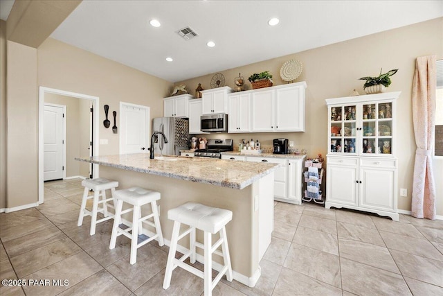 kitchen with white cabinetry, a breakfast bar, an island with sink, and appliances with stainless steel finishes