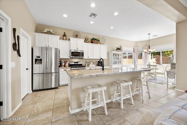 kitchen with appliances with stainless steel finishes, light tile patterned floors, white cabinetry, and a kitchen island with sink