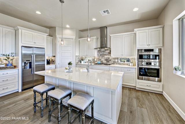 kitchen with appliances with stainless steel finishes, light stone counters, sink, wall chimney range hood, and pendant lighting