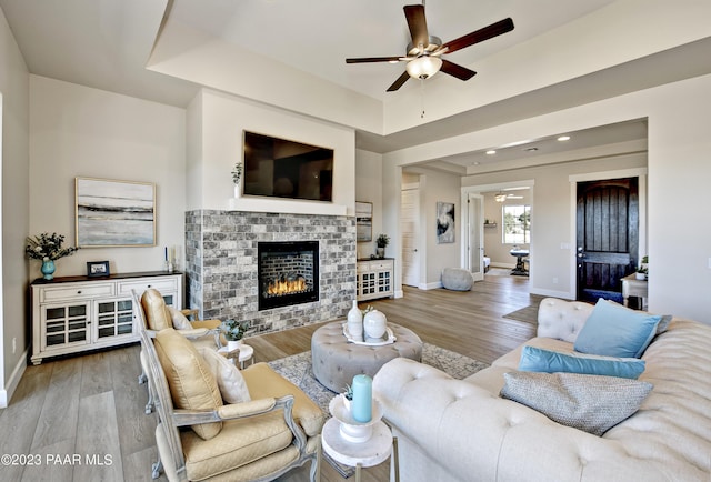 living room featuring light hardwood / wood-style flooring, ceiling fan, and a stone fireplace