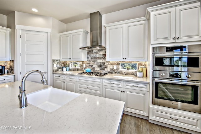 kitchen featuring sink, white cabinets, and wall chimney range hood