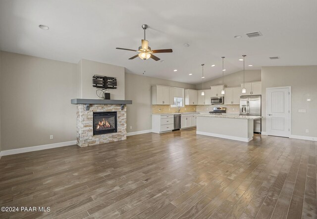 unfurnished living room with wood-type flooring, vaulted ceiling, a stone fireplace, and ceiling fan