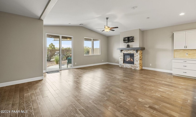 unfurnished living room with vaulted ceiling, light hardwood / wood-style floors, a stone fireplace, and ceiling fan