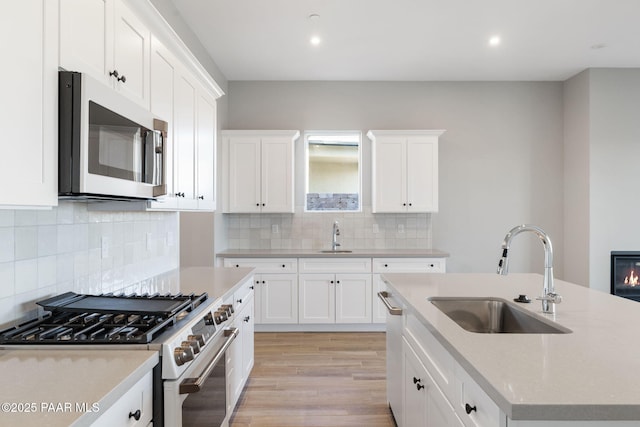 kitchen with sink, appliances with stainless steel finishes, white cabinetry, light hardwood / wood-style floors, and a center island with sink