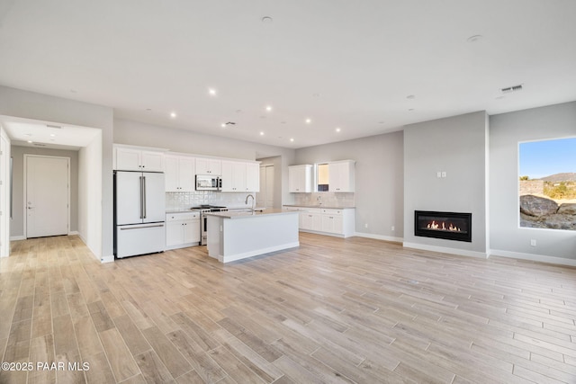 kitchen with premium appliances, backsplash, light hardwood / wood-style floors, and white cabinets