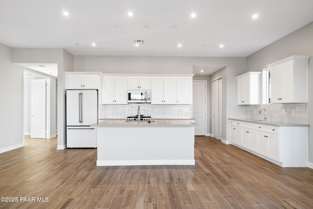 kitchen with sink, white cabinetry, a center island with sink, light wood-type flooring, and white appliances