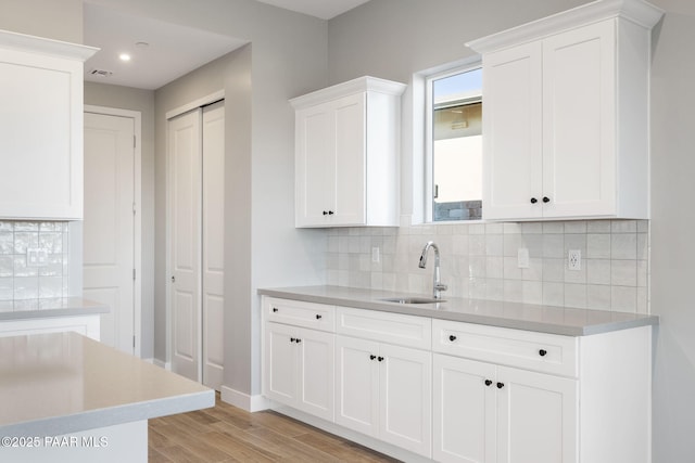 kitchen with tasteful backsplash, sink, white cabinets, and light wood-type flooring