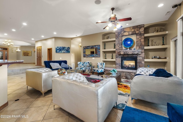 tiled living room with built in shelves, a stone fireplace, and ceiling fan with notable chandelier