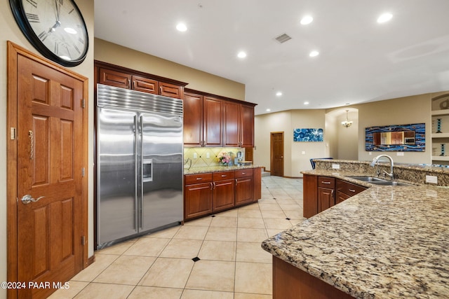 kitchen featuring light stone countertops, sink, built in refrigerator, decorative backsplash, and light tile patterned floors