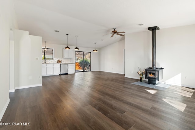 unfurnished living room with a wood stove, ceiling fan, dark wood-type flooring, and vaulted ceiling