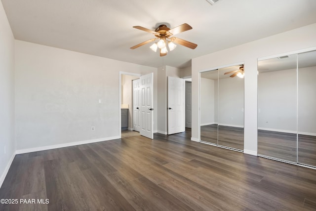 unfurnished bedroom with ceiling fan, dark hardwood / wood-style flooring, ensuite bathroom, and two closets