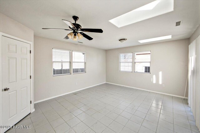 tiled empty room featuring ceiling fan and a skylight