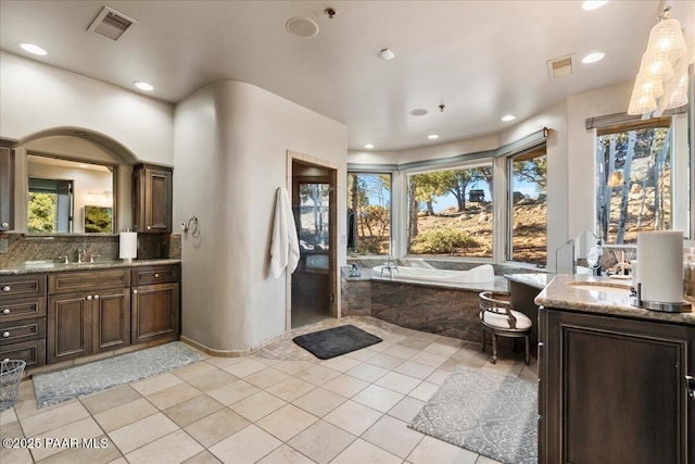 bathroom featuring a relaxing tiled tub, vanity, tasteful backsplash, and tile patterned floors