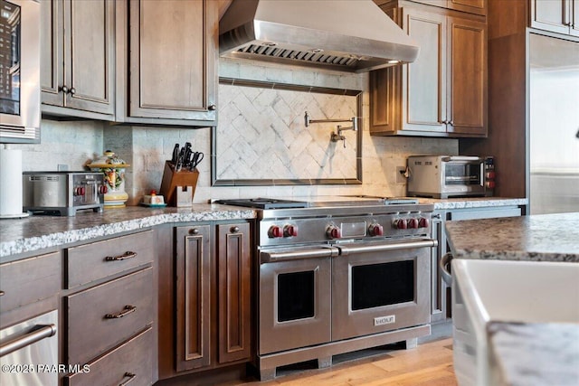 kitchen with range with two ovens, custom exhaust hood, tasteful backsplash, and light hardwood / wood-style flooring