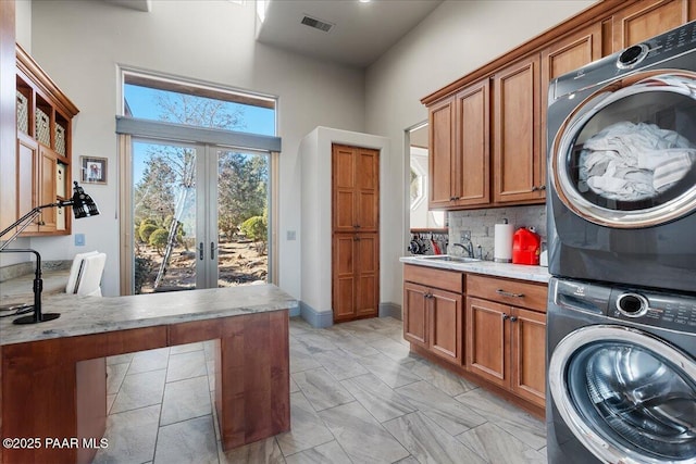 clothes washing area featuring cabinets, stacked washing maching and dryer, sink, and french doors