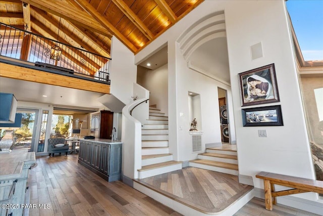 stairs with stacked washing maching and dryer, hardwood / wood-style floors, high vaulted ceiling, beamed ceiling, and wooden ceiling