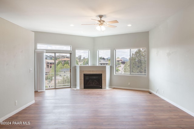 unfurnished living room featuring a tiled fireplace, ceiling fan, and hardwood / wood-style floors