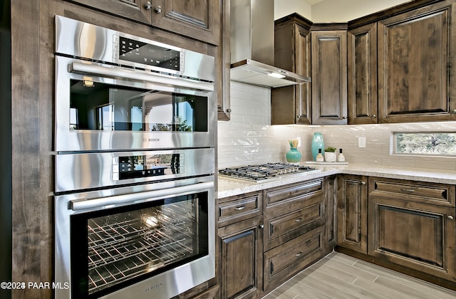 kitchen featuring tasteful backsplash, light stone countertops, appliances with stainless steel finishes, and wall chimney exhaust hood