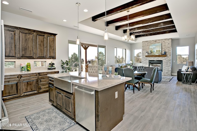 kitchen featuring pendant lighting, dishwasher, sink, light stone countertops, and a center island with sink