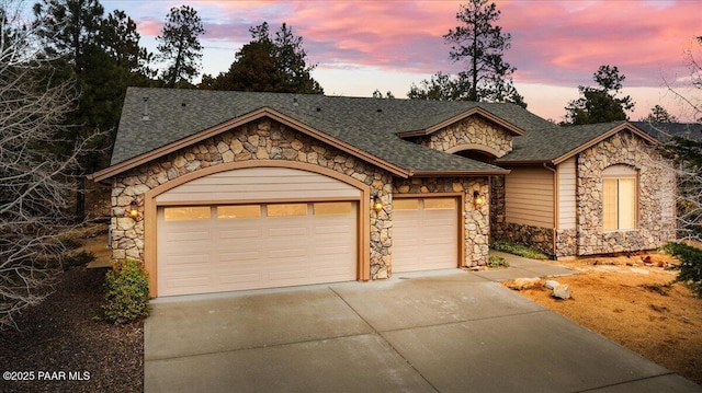 view of front of home with concrete driveway, an attached garage, stone siding, and a shingled roof