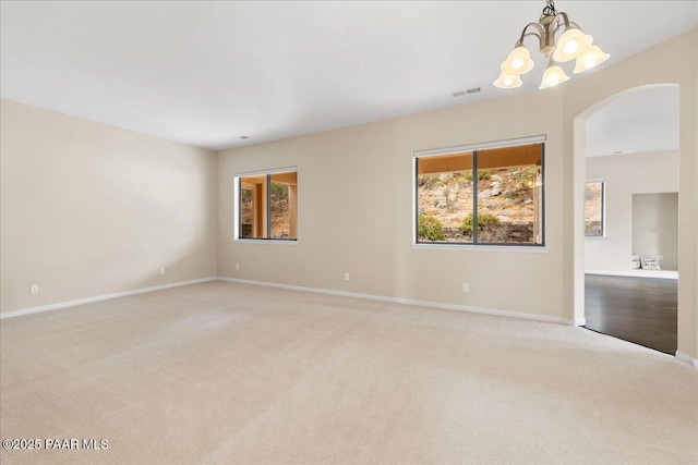 unfurnished room featuring baseboards, visible vents, an inviting chandelier, arched walkways, and light carpet