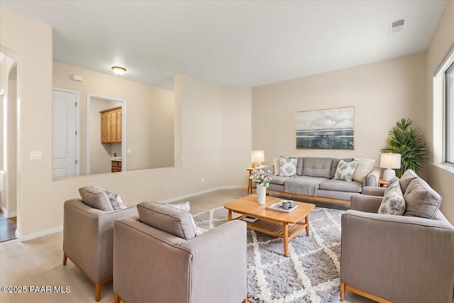 living area with light wood-style flooring, baseboards, visible vents, and arched walkways