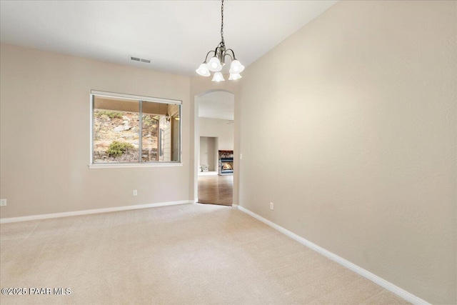 unfurnished room with visible vents, baseboards, arched walkways, light colored carpet, and a chandelier